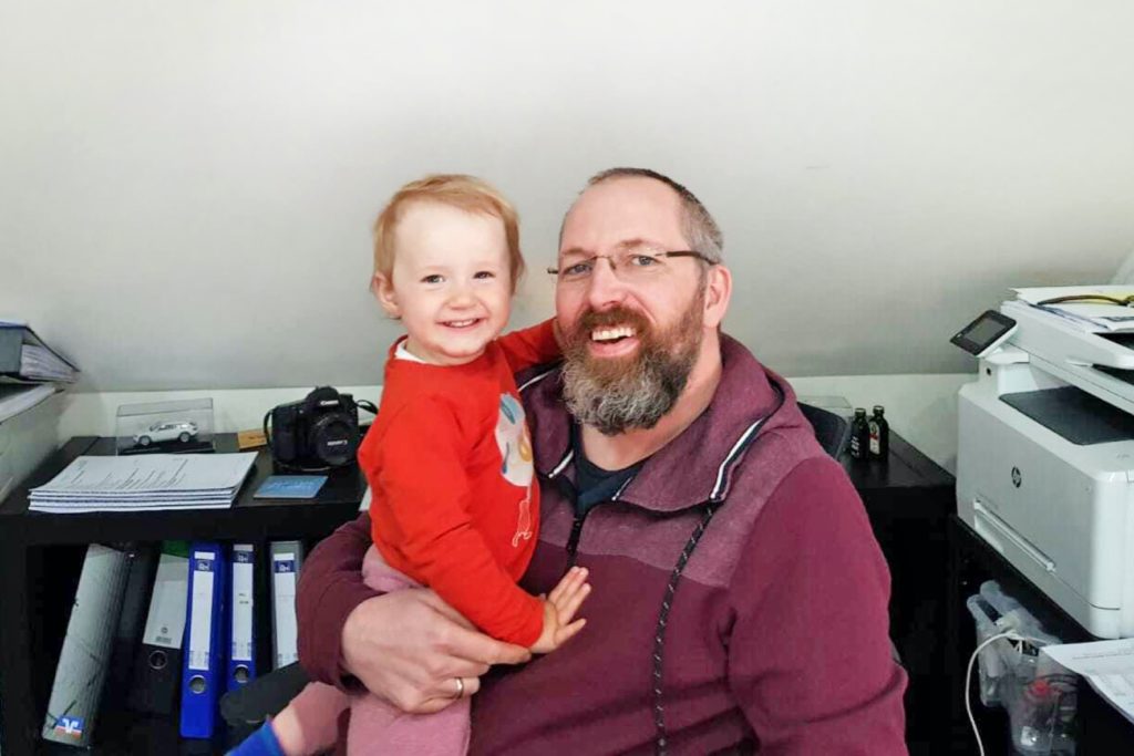 Alex Frison mit seiner kleinen Tochter im Arm im eigenen Home Office