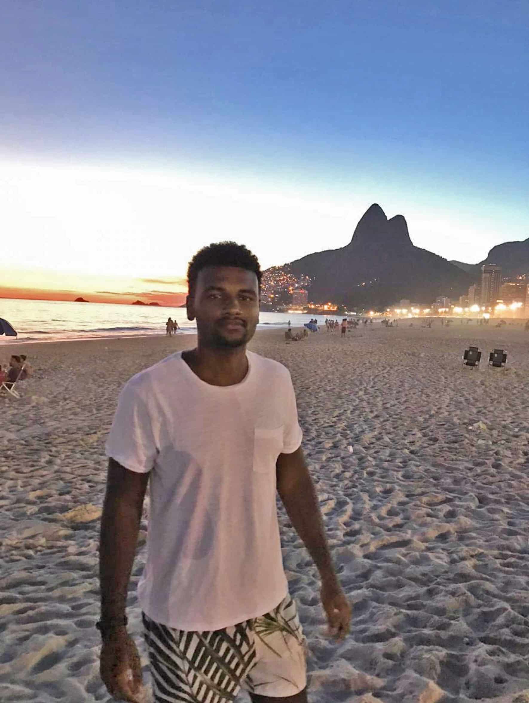 This picture shows Matheus at sunset on the beach in Rio de Janeiro. In the background there are the lights of the city.